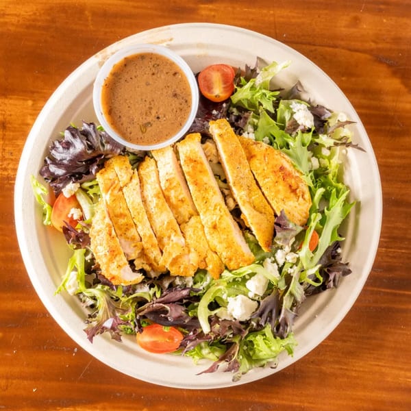 Grilled chicken salad with mixed greens, cherry tomatoes, feta cheese, and a side of dressing.