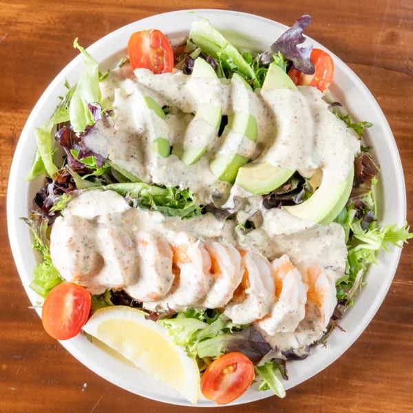 Shrimp and avocado salad with cherry tomatoes, lemon, and creamy dressing in a white bowl.