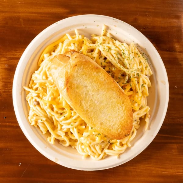 Creamy pasta with shredded cheese and a golden-brown piece of garlic bread on a white plate.