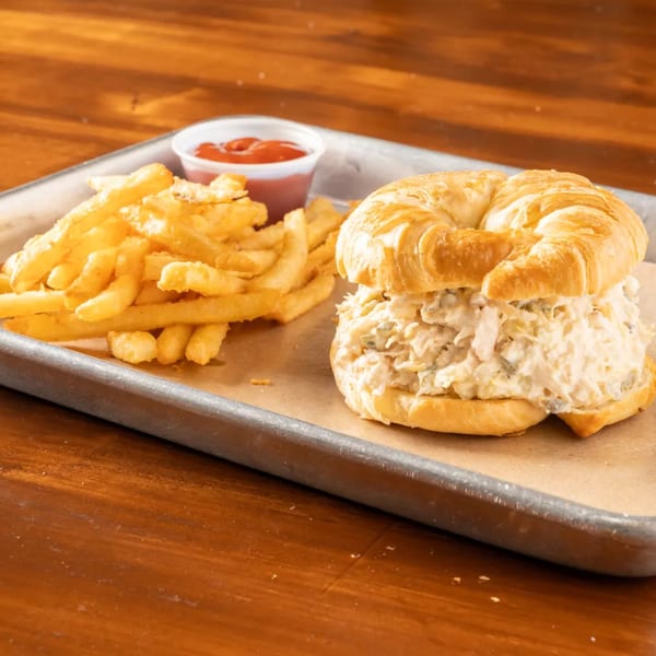 Chicken salad croissant sandwich with a side of french fries and ketchup on a metal tray.
