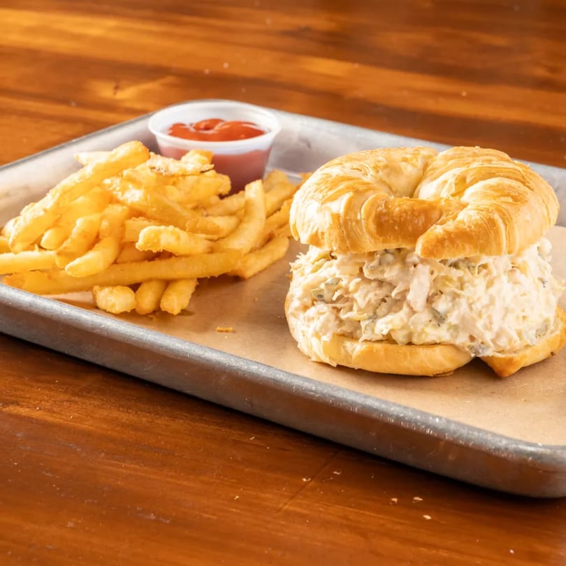 Chicken salad croissant sandwich with a side of french fries and ketchup on a metal tray.