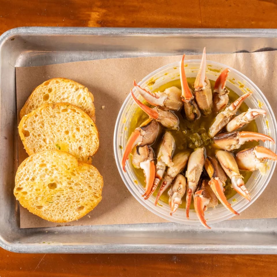 Stone crab claws in a clear container with sauce, next to three slices of toasted bread.