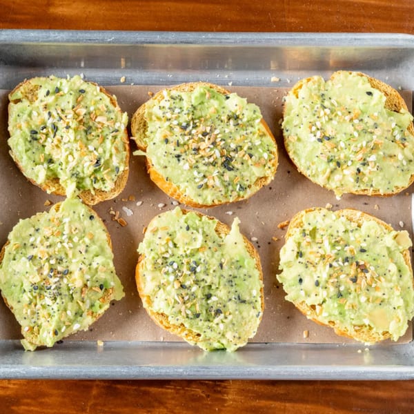 Six pieces of avocado toast with everything bagel seasoning on a baking sheet.