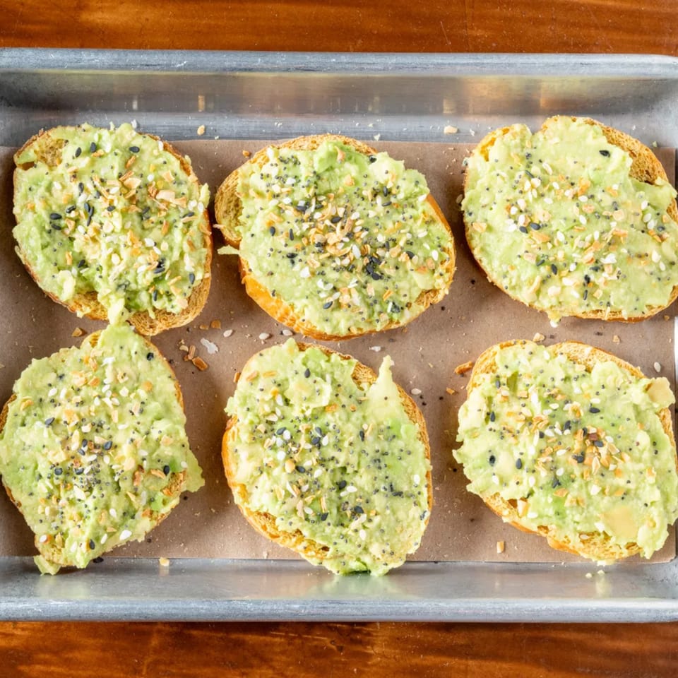 Six pieces of avocado toast with everything bagel seasoning on a baking sheet.