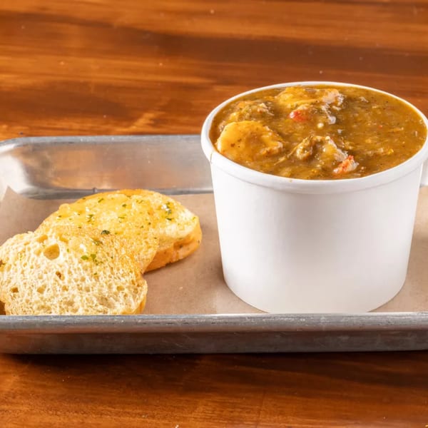 A white cup of gumbo with shrimp and vegetables, served with two slices of garlic bread.
