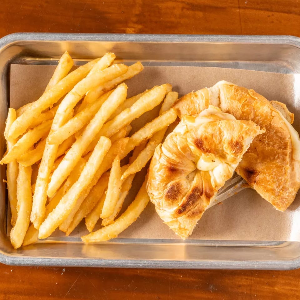 Golden french fries and two cheesy, toasted croissants on a metal tray with parchment paper.
