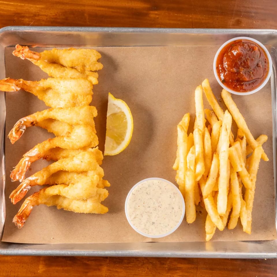Fried shrimp, french fries, a lemon wedge, and two dipping sauces on a metal tray.